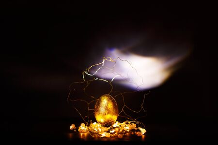 Precious easter golden egg in gold decorations over dark background, magic of easter concept, defocused lightsの写真素材