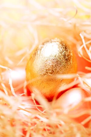 Light happy easter background, golden colored eggs in hay nest close-up, pastel colorsの写真素材
