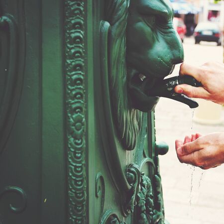 Male hands close-up, unrecognizable tourist washing hands in street fountain in old town of Europe, image tonedの写真素材