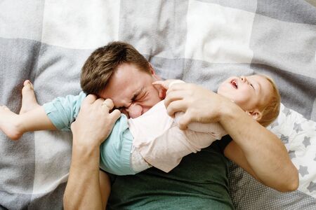 Top view of affectionate young father holding his baby daughter kid and tickling her, father`s day concept, loving family の写真素材