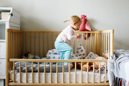 Cute funny little toddler girl playing in a crib in bedroomの写真素材