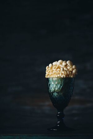 Enoki, Enokitake, Flammulina velutipes, edible mushroom popular in Japanese cuisine. Still life with little white mushrooms putted in blue wine glass on dark background.の写真素材
