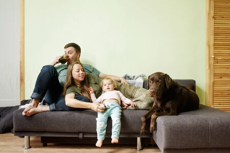 Young happy family with little toddler kid and dog labrador retriever at home on the couch, stay home concept, full body, real peopleの写真素材