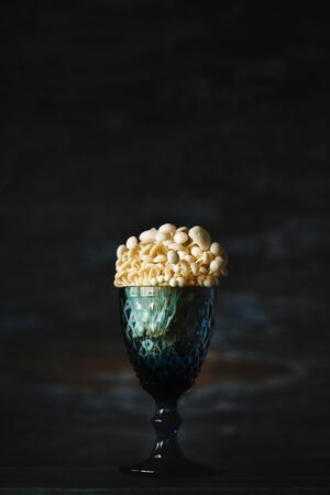 Enoki, Enokitake, Flammulina velutipes, edible mushroom popular in Japanese cuisine. Still life with little white mushrooms putted in blue wine glass on dark background.の写真素材
