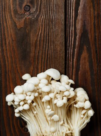 Enoki,  Enokitake, Flammulina velutipes, edible mushroom popular in Japanese cuisine. Heap of little white mushrooms served on wooden brown background close-up.の写真素材