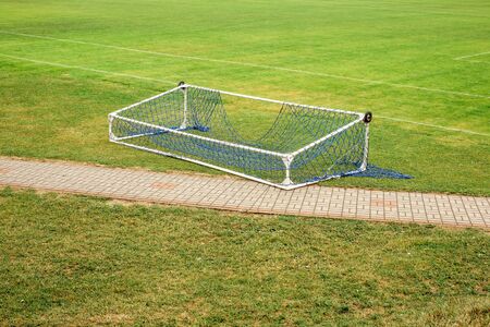 Abandoned fallen soccer football gate lying on empty green fieldの写真素材