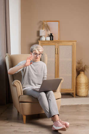 Young trendy woman in casual cloth talking by the mobile cell phone working on laptop from homeの写真素材