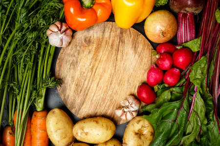 Frame made of fresh assorted vegetables around wooden round cutting board close upの写真素材