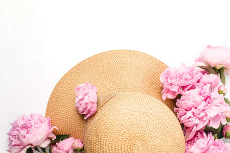 Summer holiday concept, straw braided hat, pink peony flowers on white background, top view. Vacation and travel banner.の写真素材
