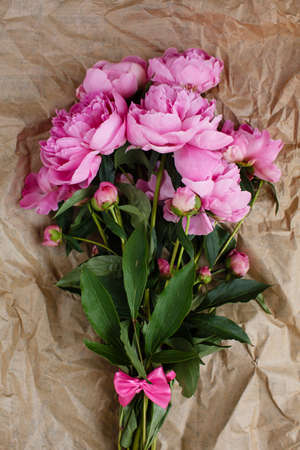 Fluffy bouquet of pink peonies flowers in sunlight on wrinkled craft paper background, top viewの写真素材