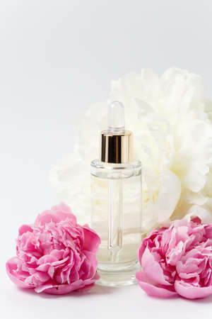 Glass transparent mockup bottle with dropper with cosmetic serum, oil, essence among pink and white peony flowers on white backgroundの写真素材