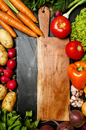 Frame made of fresh ripe assorted vegetables around cutting board close up: tomatoes, carrots, peppers, beets, carrots, garlicの写真素材