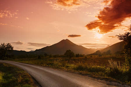 Amazing mountain landscape with vibrant sunset and country road, travel backgroundの写真素材