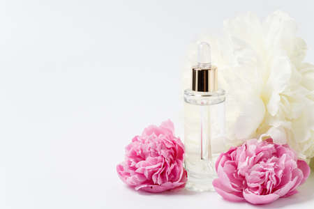 Glass transparent mockup bottle with dropper with cosmetic serum, oil, essence among pink and white peony flowers on white backgroundの写真素材
