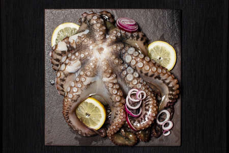 Seafood, whole raw big octopus on a stone dish served with lemon and red onion ready for cooking, view from aboveの写真素材
