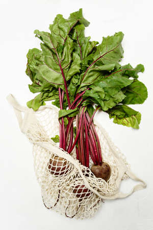 Trendy string bag with fresh young beetroot and haulm over light white background. Zero waste sustainable lifestyle concept.の写真素材