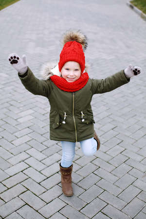 Sweet little funny girl in trendy outfit walking and dancing on the street, having fun, waving hands, full body looking at cameraの写真素材