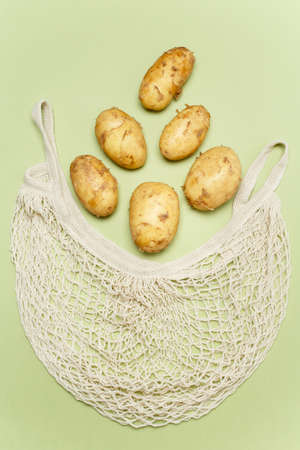 Trendy string bag with fresh young potatoes inside over light green background. Zero waste sustainable lifestyle concept.の写真素材