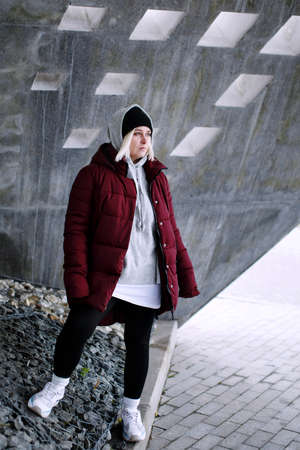 Young millennial hipster teenager female portrait, blonde young woman in a black hat standing outdoors over gray urban wall looking away, full bodyの写真素材