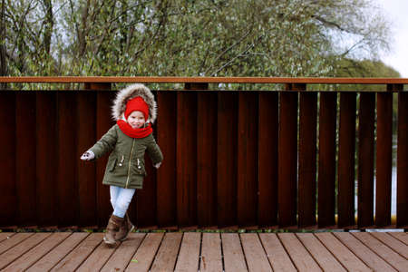 Cute little girl in warm outerwear dancing and having fun on the street in fall or wintertime, full bodyの写真素材