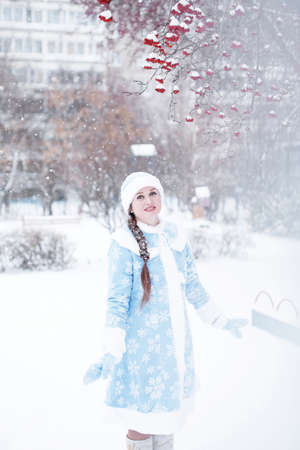 Beautiful young woman in traditional russian suit of snow maiden, new year and christmas holiday girl posing outdoors in snowy weatherの写真素材