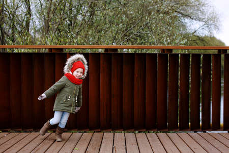 Cute little girl in warm outerwear dancing and having fun on the street in fall or wintertime, full bodyの写真素材