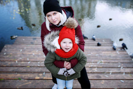 Young mother walking with her cute little daughter outside in urban park near riverの写真素材