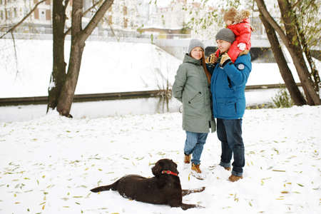 Full height portrait of happy family with one kid and dog in winter casual oufit posing outdoors in snow public parkの写真素材