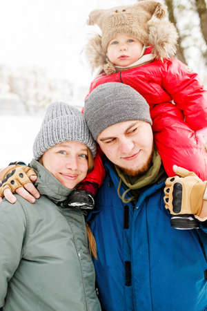 Close-up portrait of young happy family with one toddler in winter casual oufit posing outdoors in snowy public parkの写真素材