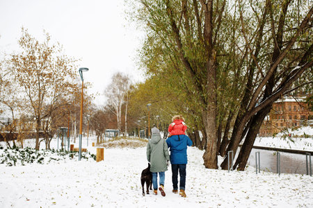 Full height of happy family with one toddler in winter casual outfit having fun outdoors sitting on a bench swing in snow public parkの写真素材