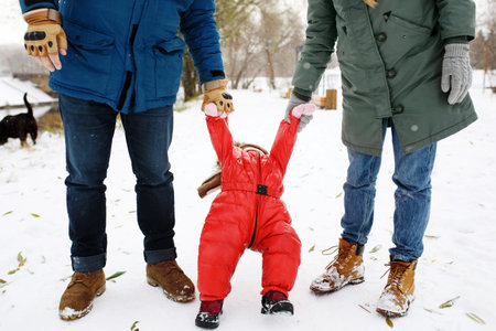 Full height of happy family with one toddler in winter casual outfit having fun outdoors sitting on a bench swing in snow public parkの写真素材