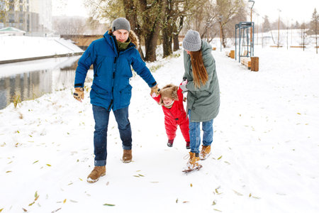 Full height of happy family with one toddler in winter casual outfit having fun outdoors sitting on...