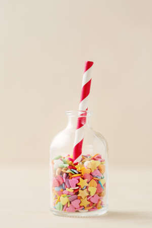 Colorful heart and star sprinkling in a little bottle with striped red and white straw, selective focusの写真素材