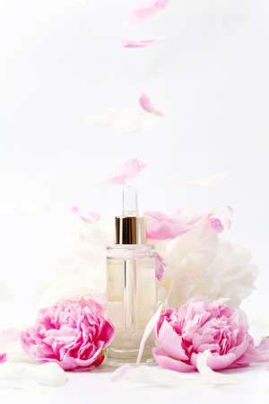 Glass transparent mockup bottle with dropper with cosmetic serum, oil, essence among pink and white peony flowers on white background, valentine`s day giftの写真素材