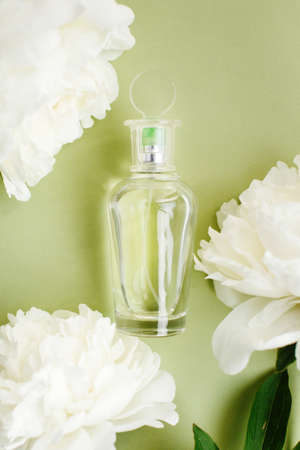 Transparent mockup glass bottle with perfume among fresh white peony flowers on olive green pastel color, top viewの写真素材