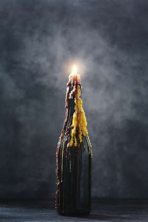Burning candle with melted wax in a bottle on dark background, halloween decoration with mystical lightの写真素材