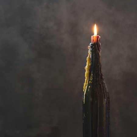 Burning candle with melted wax in a bottle on dark background, halloween decoration with mystical lightの写真素材
