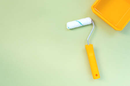 New painting roller and yellow paint tray on pastel green background top view flat layの写真素材