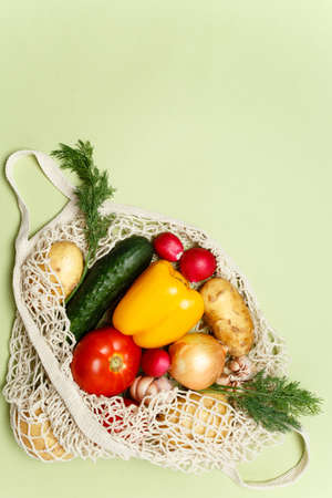 Trendy string bag with fresh vegetables and greens over light green background: potatoes, tomatoes, onion, bell pepper. Zero waste sustainable lifestyle concept.の写真素材