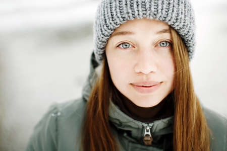 Beautiful calm smiling young woman in winter warm outfit posing outdoors in snowy park, close-up portrait looking at cameraの写真素材
