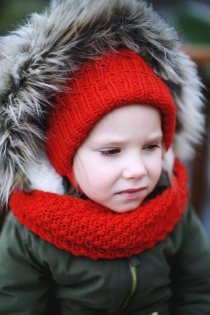 Portrait of cute sad little girl in warm outerwear clothing outdoors alone in cool weather in wintertime close-upの写真素材
