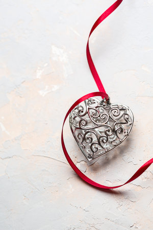 Saint Valentine day greeting card, beautiful silver heart with red ribbon on gray textured backgroundの写真素材