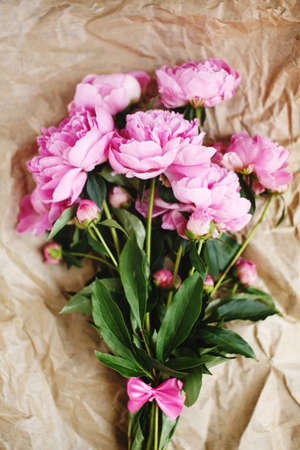 Tender bouquet of pink peonies flowers in sunlight on wrinkled craft paper background, top view, Valentine`s dayの写真素材