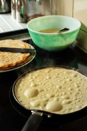 A thin homemade pancake (crepe) is frying in a black skillet with olive oil. The vertical shot...