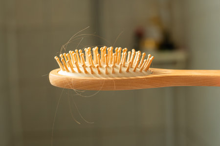 A close-up of a wooden hairbrush with loose strands caught in its bristles, set against a soft...