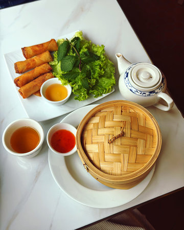 Asian lunch featuring aromatic tea, crispy spring rolls, fresh lettuce, and traditional dim sum in a...