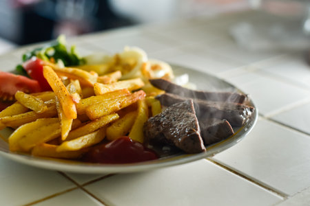Quality photo of a homemade lunch featuring hot, steaming steak, golden french fries, and fresh tomato salad. Emphasizes balanced nutrition and quality organic ingredients.の写真素材