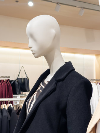 Stylish mannequin showcasing a modern autumn-winter fashion look with a black coat and animal print top. Highlights contemporary trends in retail display. Vertical photo.の写真素材