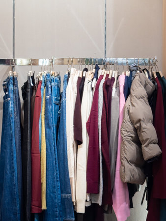 Diverse range of modern autumn and winter fashion items on a retail rack. Showcases current trends in casual wear, including denim and outerwear for the season. Vertical photo.の写真素材