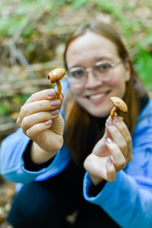 Happy girl holding two wild mushrooms in autumn forest. Emphasizes the importance of mushroom...